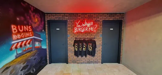 Neon sign reading You wanna burger me above Buns and Guns t-shirts
